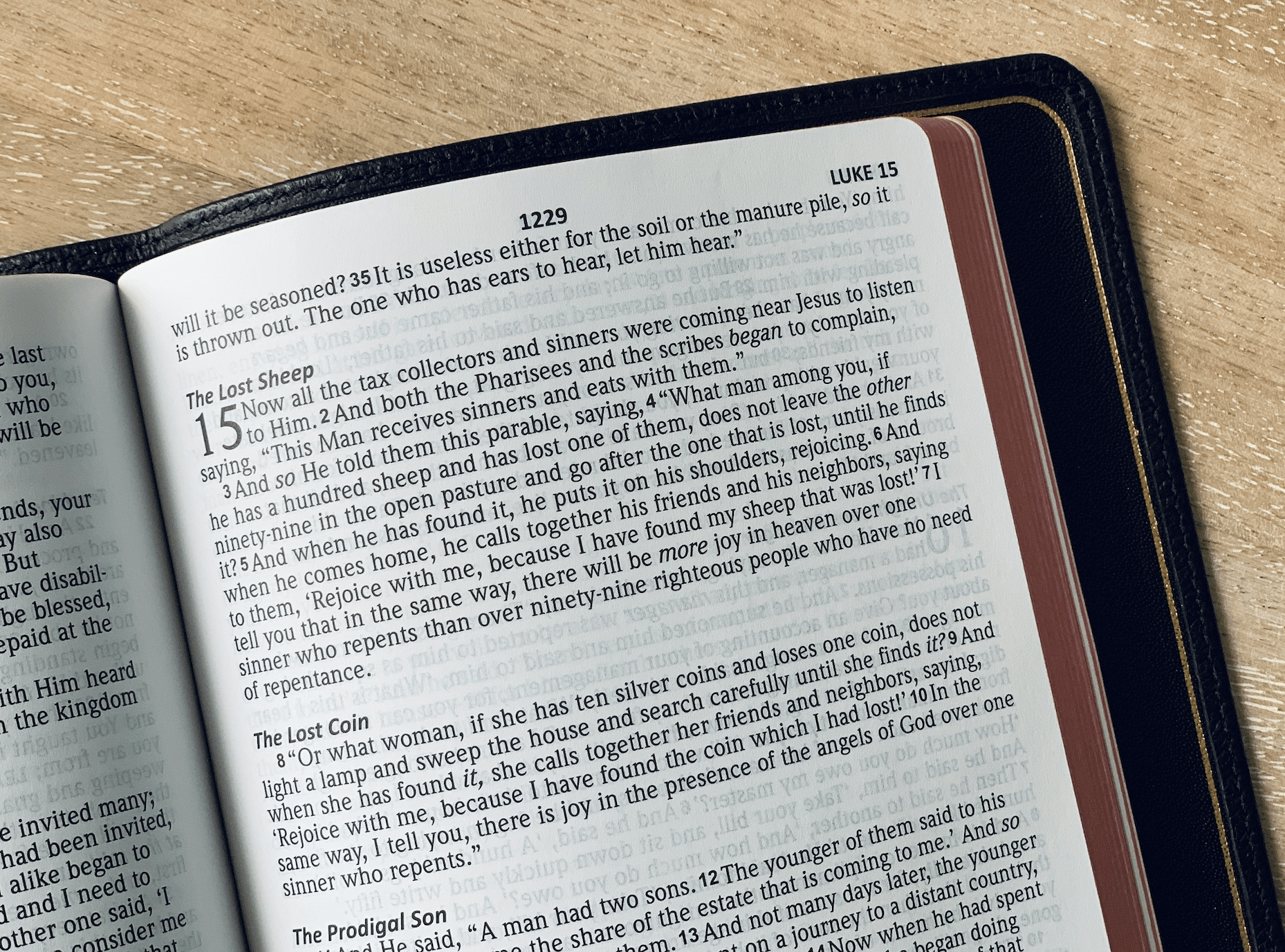 Open Bible on a wooden table, page showing Luke 15 and the 'The Lost Sheep' heading only.