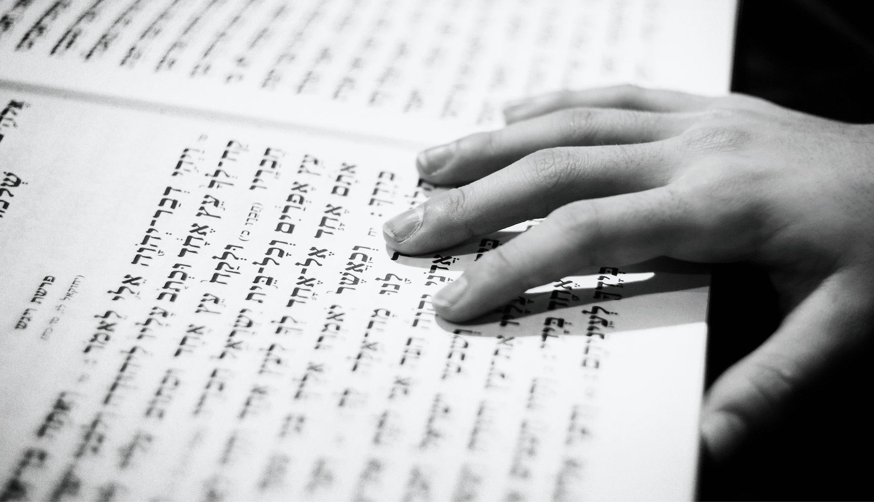 Close-up of a hand resting on a page of Hebrew text in a book.