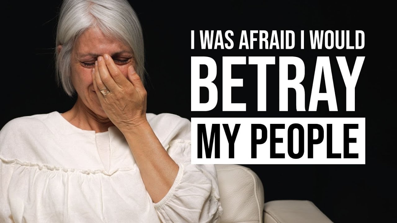 Older woman with gray hair crying, hand over her face, white blouse, on a dark background with bold text: 'I WAS AFRAID I WOULD BETRAY MY PEOPLE'