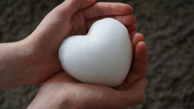 Two hands gently cup a rounded snowball outdoors against a blurred natural background.