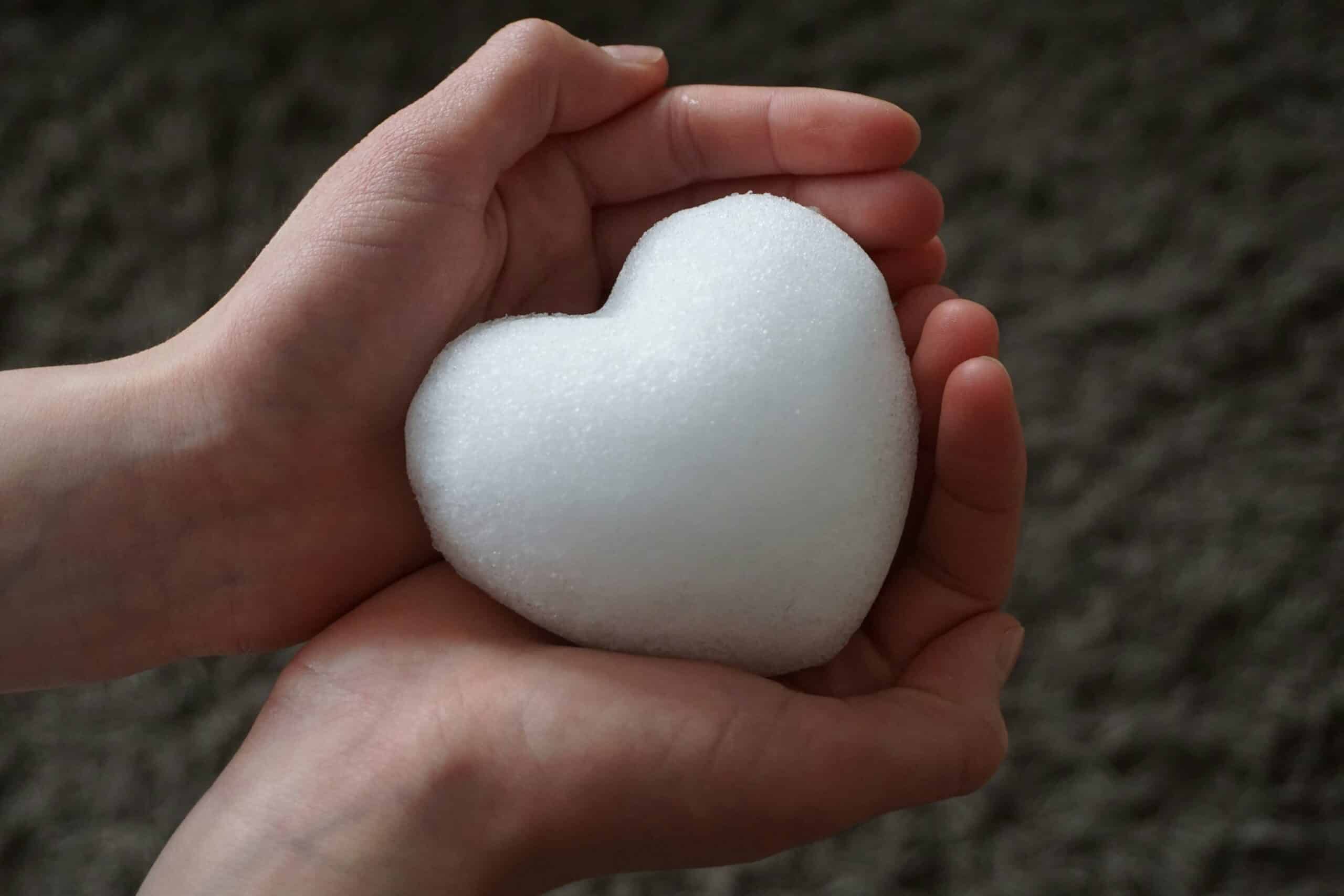 Two hands gently cup a rounded snowball outdoors against a blurred natural background.